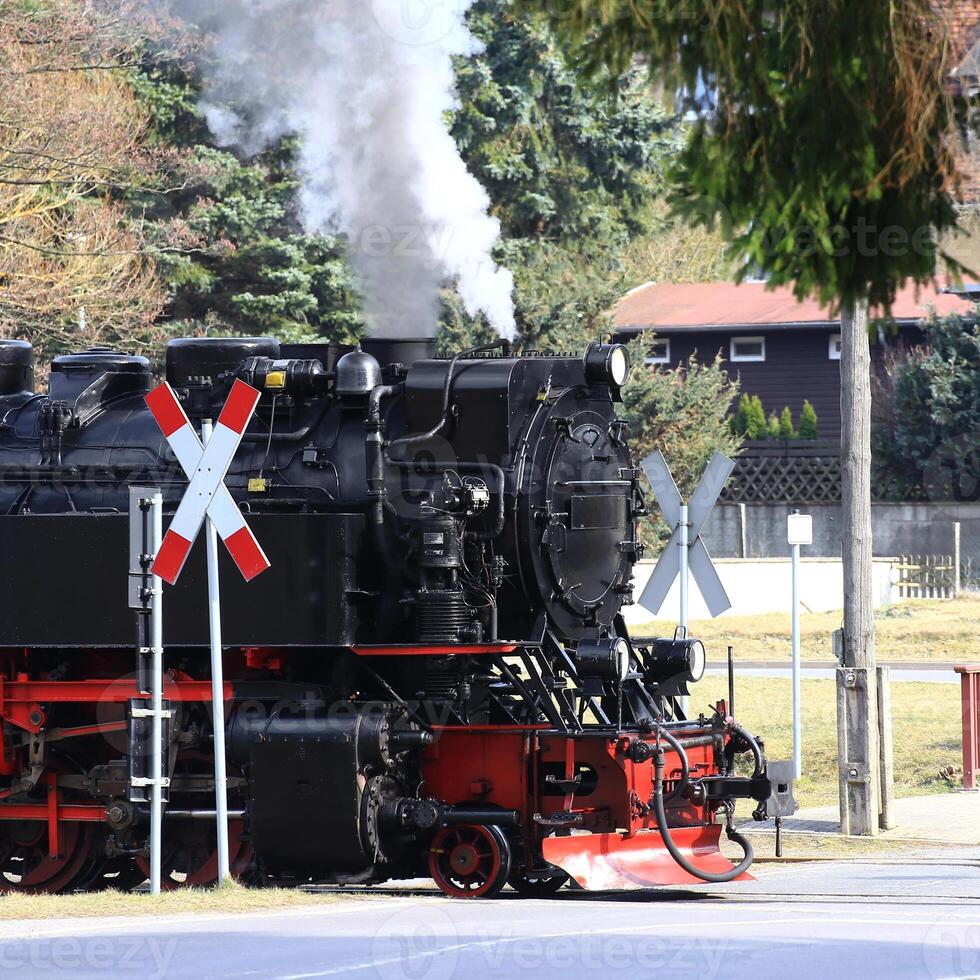 Historic steam locomotive crossing a rural railway intersection in Germany with smoke rising from its chimney photo