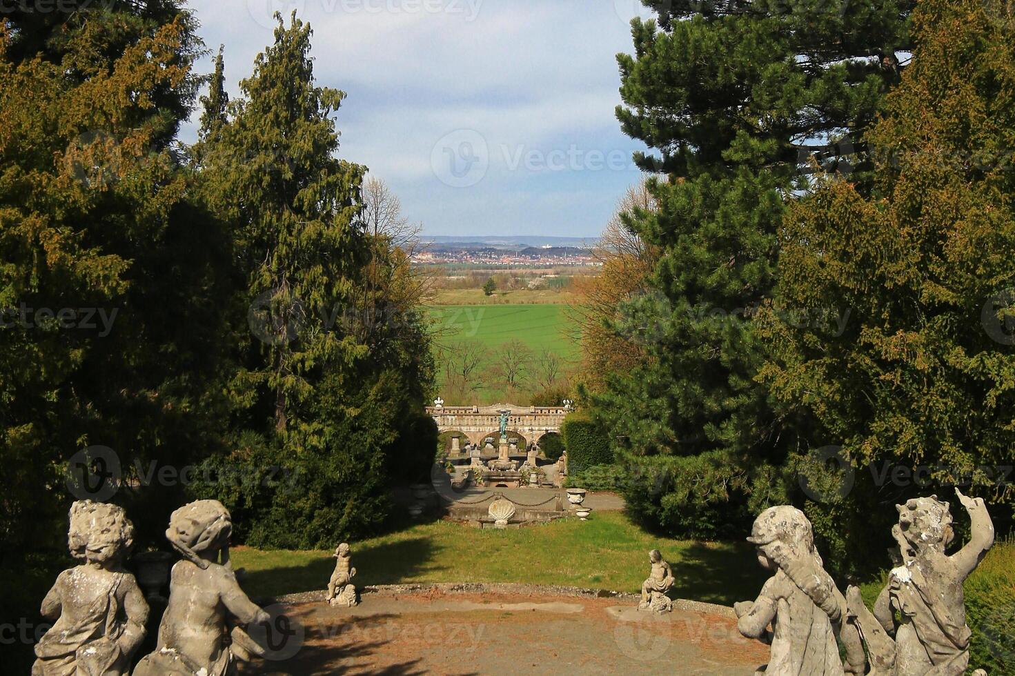 Statues framing Roseburg garden view in Germany, with distant town beyond green fields and formal tree borders photo