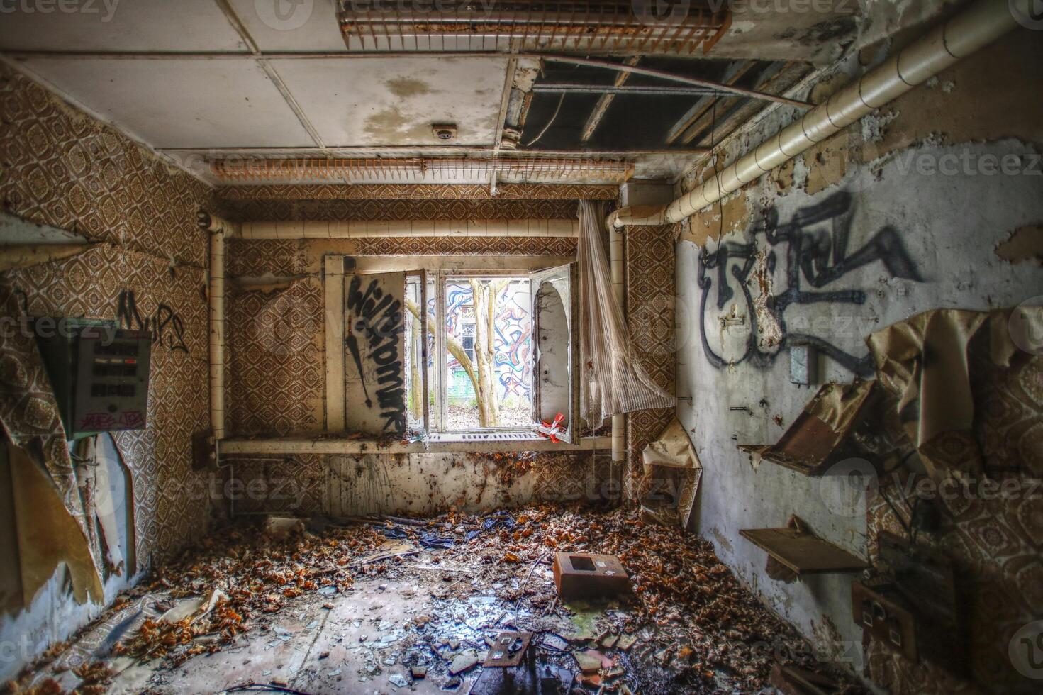 Decayed interior room with peeling wallpaper, scattered debris, graffiti, and an open window photo