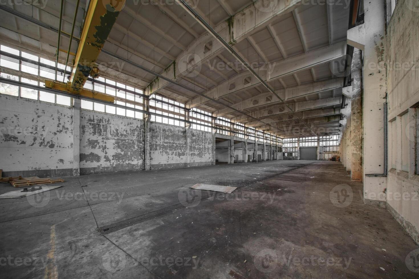 Empty factory hall with peeling walls, exposed beams, and large windows letting in dim light photo