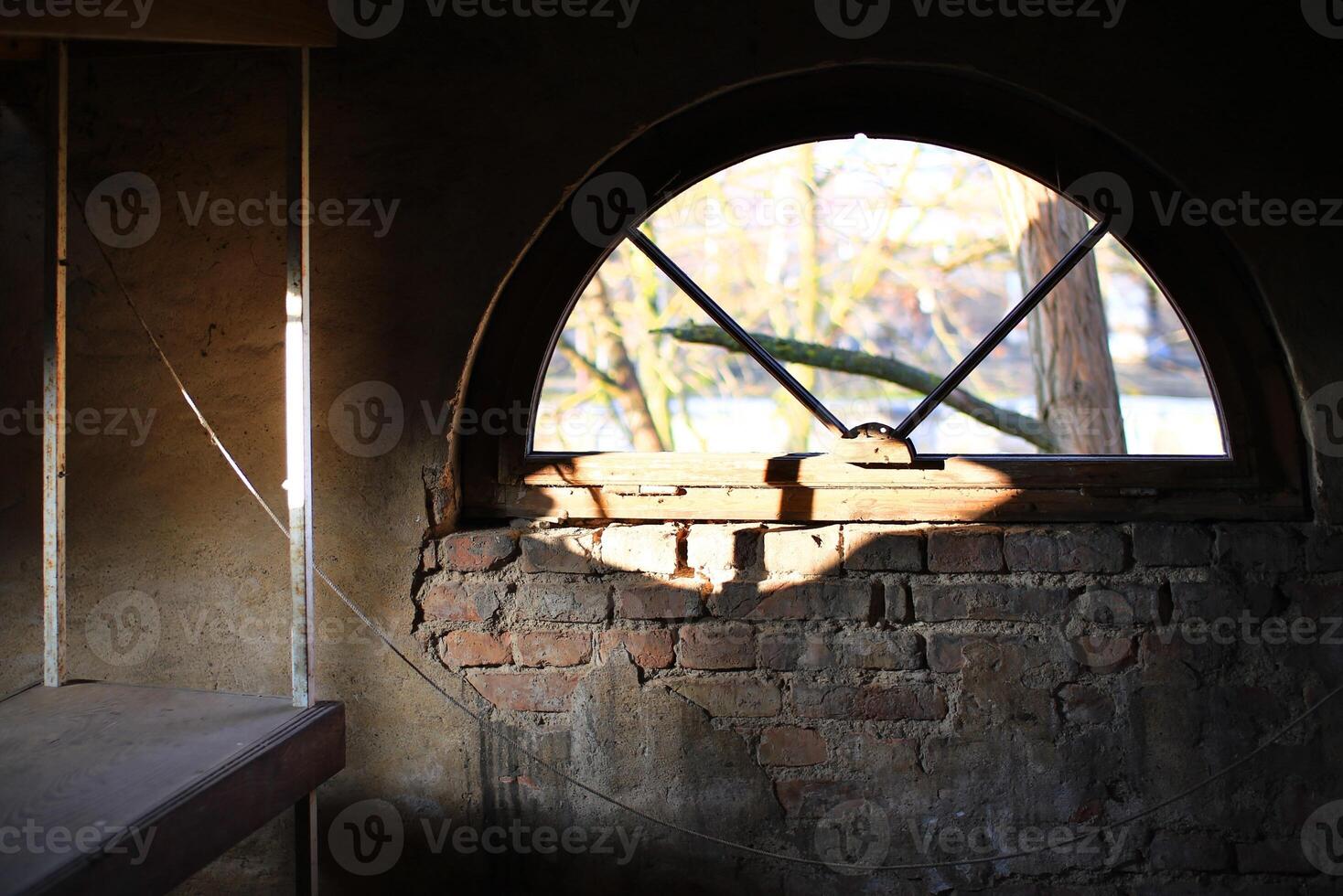 Arched brick window letting in sunlight through a broken frame with an exposed weathered wall photo