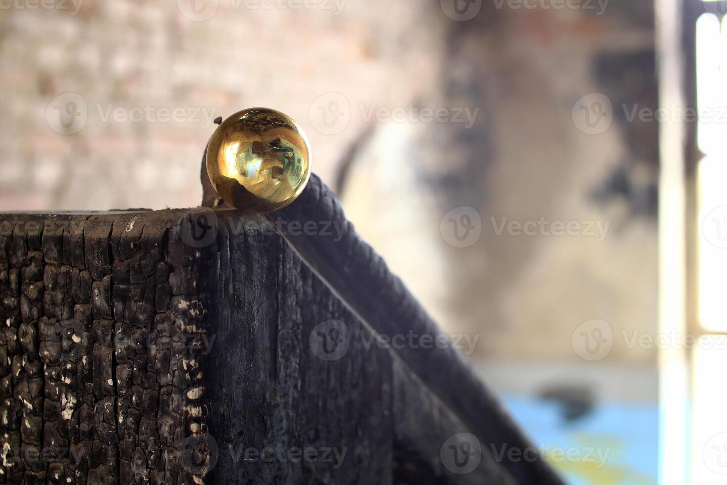 Burnt wood railing topped with brass sphere inside decayed interior space photo
