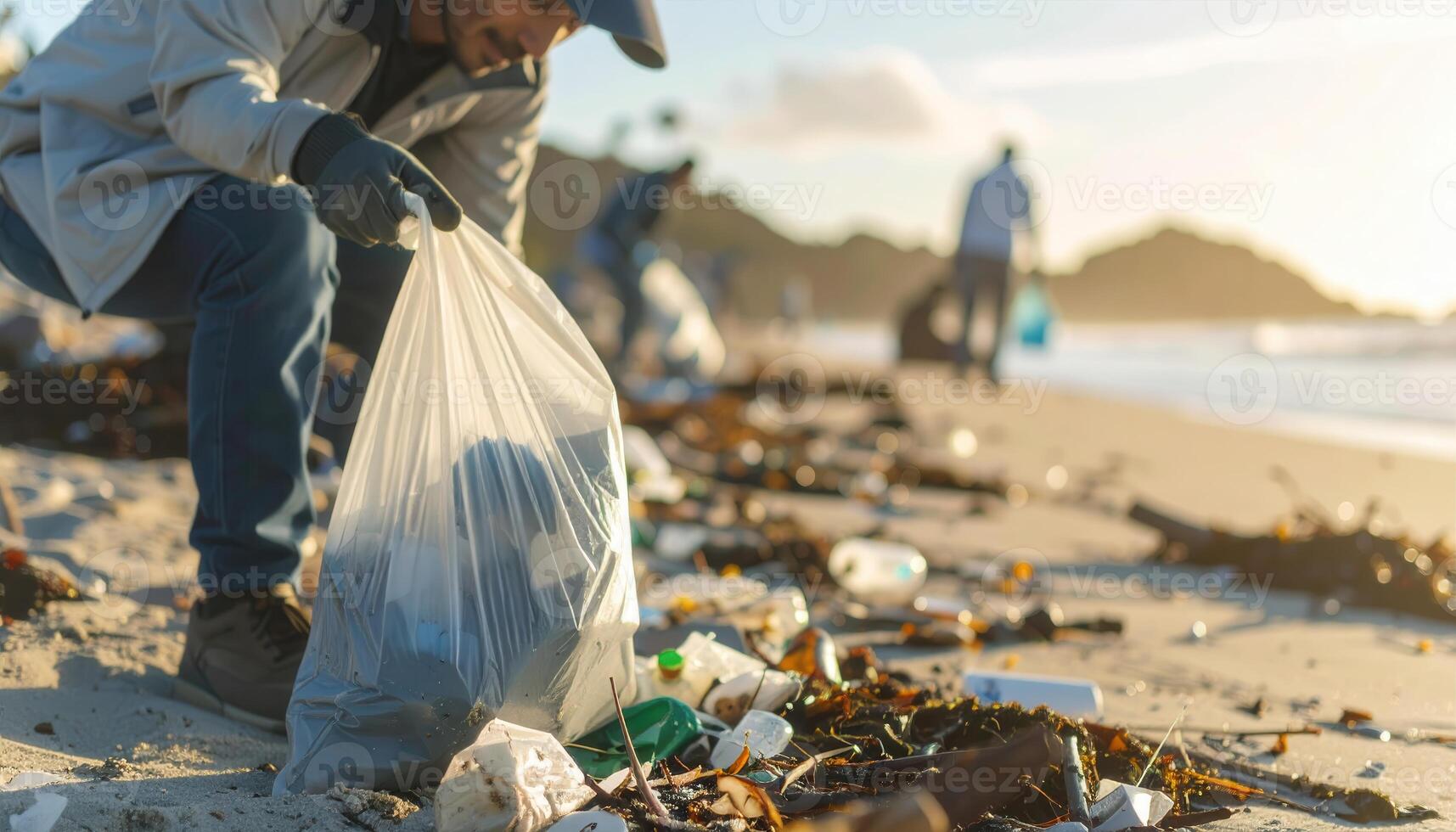 Man wearing gloves collects garbage into a plastic bag on a sandy beach. Volunteer cleans up trash and plastic waste to protect the environment. Beach cleanup concept. photo