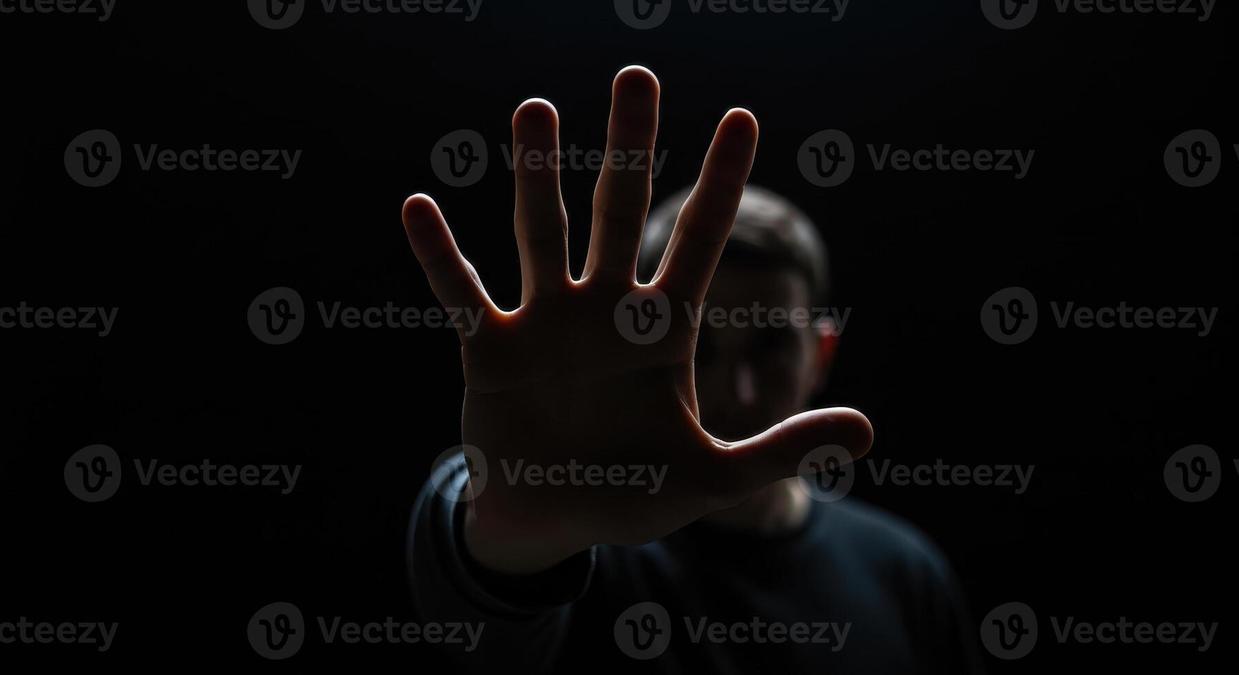 A close up shot of a hand raised towards the camera, fingers slightly spread, blocking the view of a blurred man in the background. photo