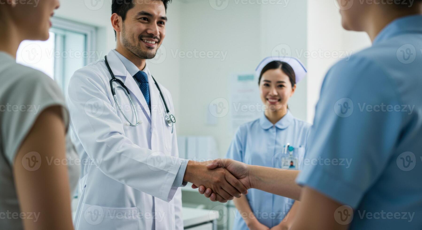 Friendly male doctor in white coat shakes hands with patient in clinic. Smiling female nurse in blue uniform stands nearby. Healthcare and medical concept. photo