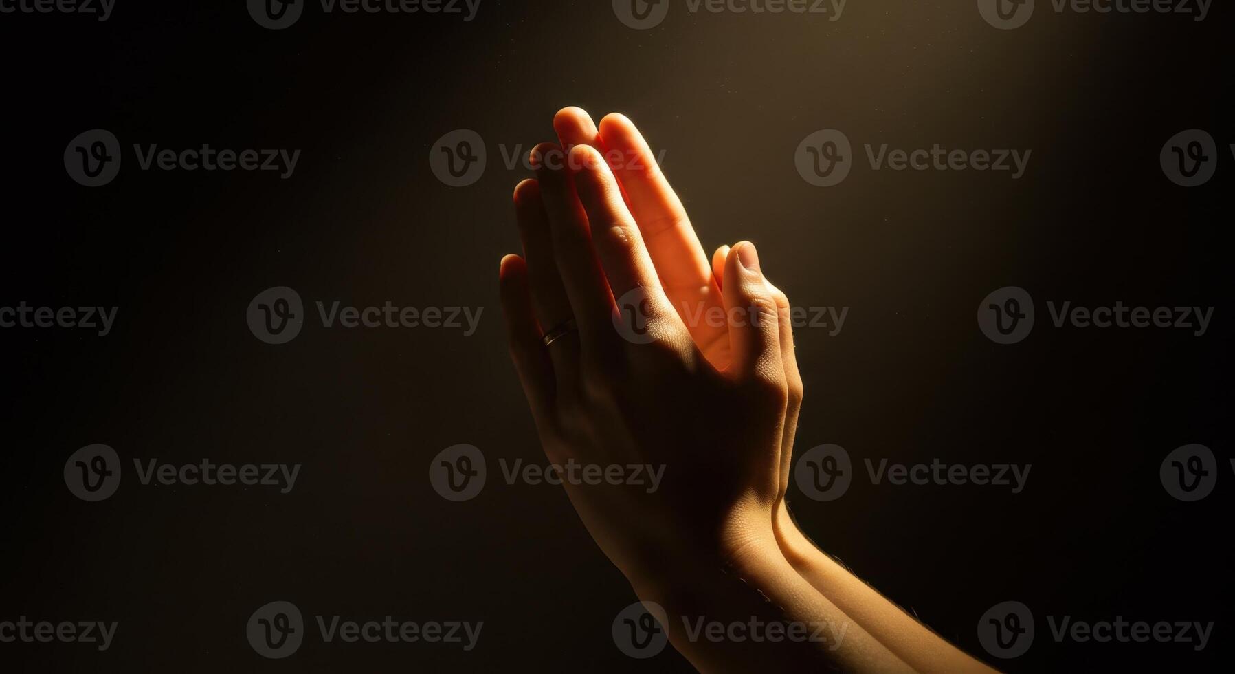 Woman hands pressed in prayer against a dark background, illuminated by soft, warm light, symbolizing faith, hope, and gratitude in a spiritual context. photo