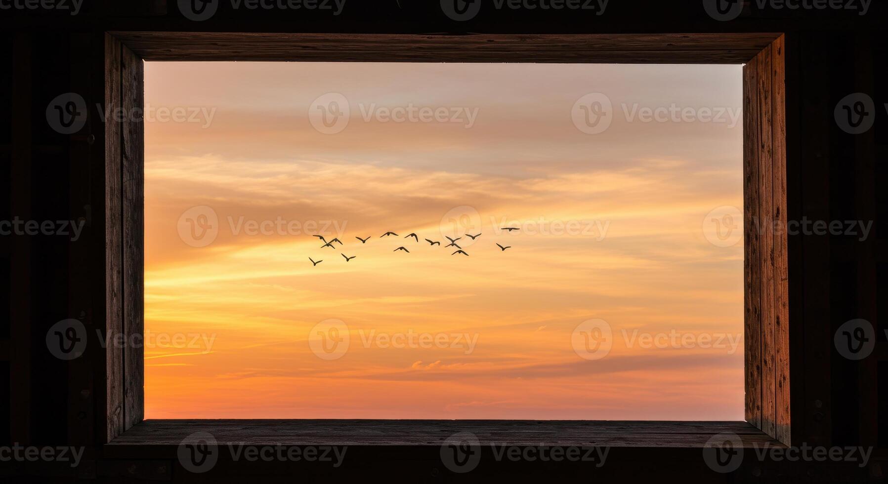 Scenic view of birds flying in formation across a vibrant orange sunset sky, framed by a rustic wooden window, creating a serene atmosphere. photo
