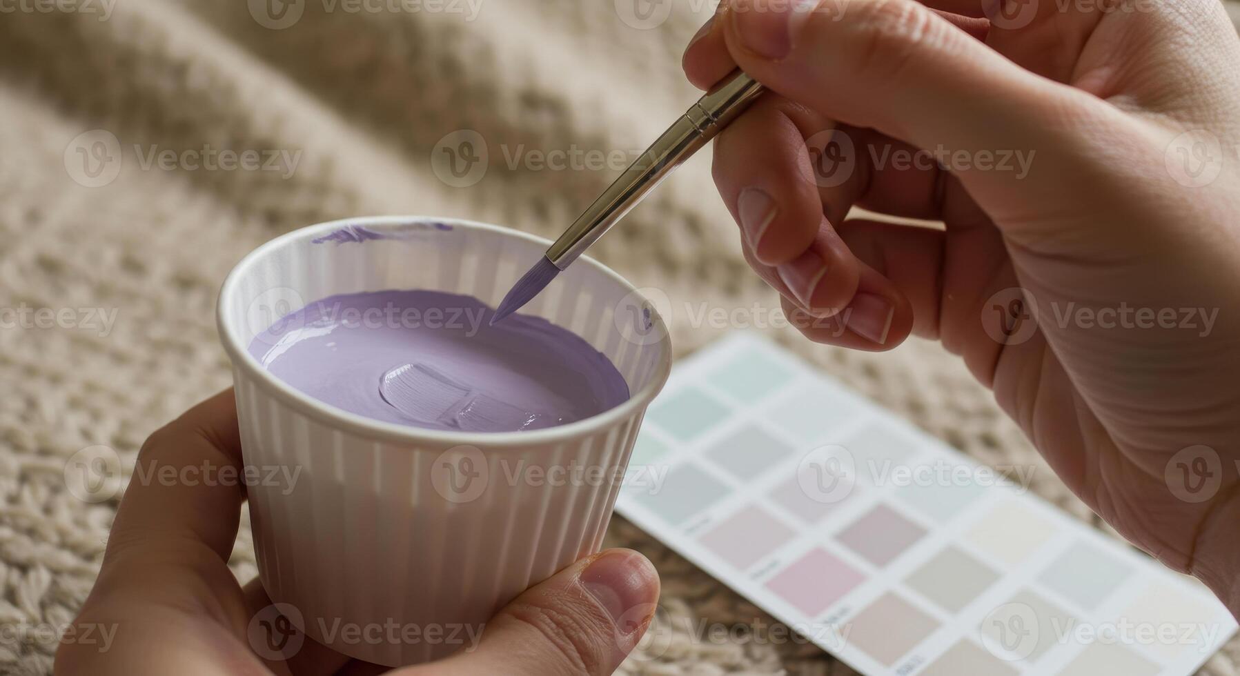 Close up on a hand holding a paint brush dipping into a cup of purple paint, with a color palette nearby, showcasing color selection. photo