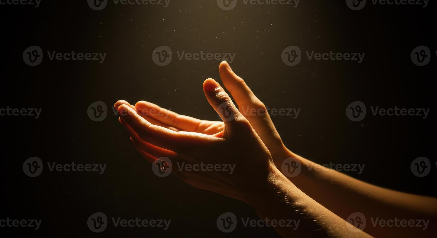 Warm light illuminates womans hands in prayer or gratitude against a dark, textured background, conveying peacefulness and spirituality. photo