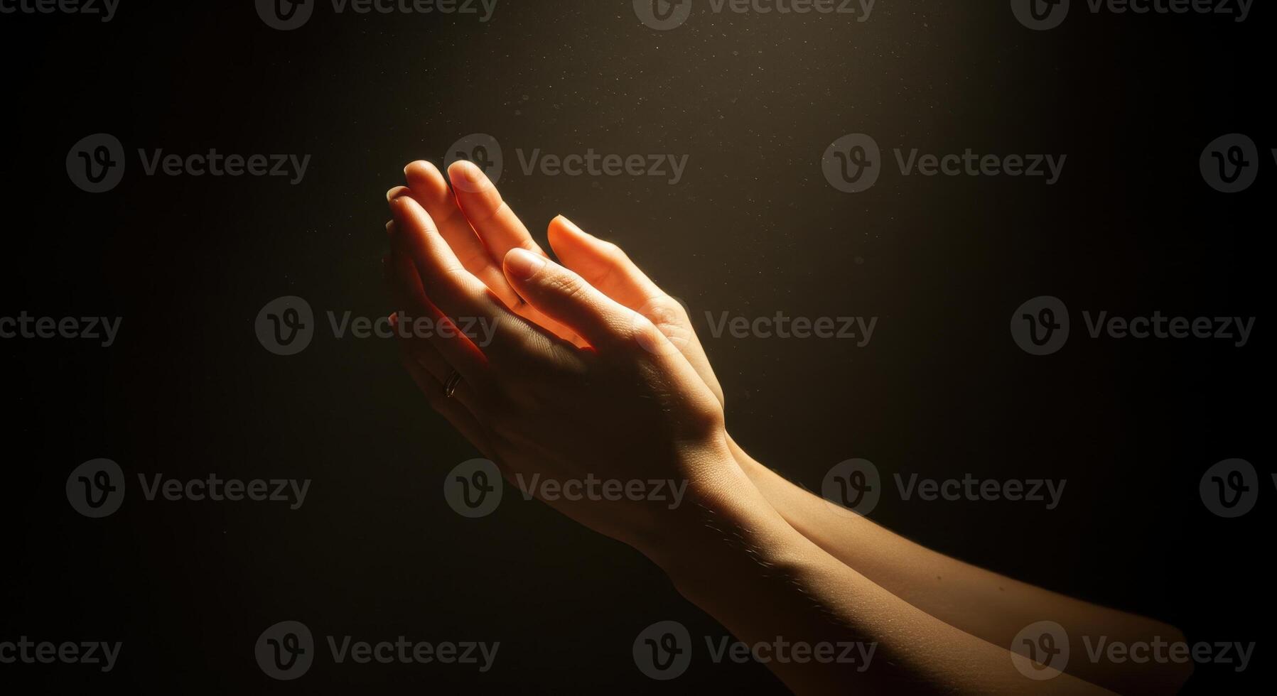 Woman hands pressed together in prayer or gratitude, illuminated by soft warm light against a dark, subtly textured background. Faith and spirituality concept. photo