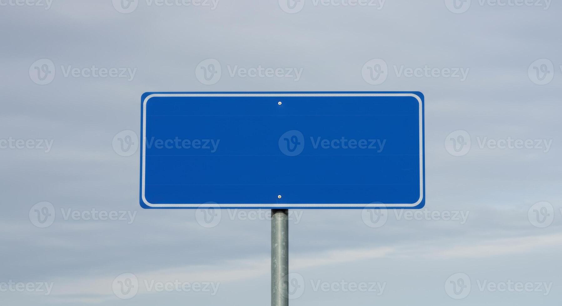 Blank rectangular blue road sign with rounded corners and white border on a gray metal post against a cloudy sky. Space for text. photo