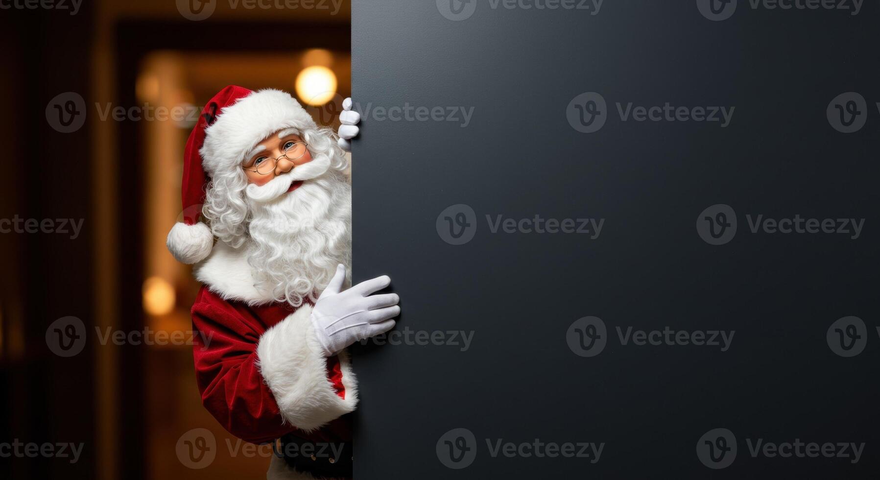 Santa Claus peeks from the left of a large vertical dark gray sign, gesturing towards the board with his right hand. Christmas concept. photo