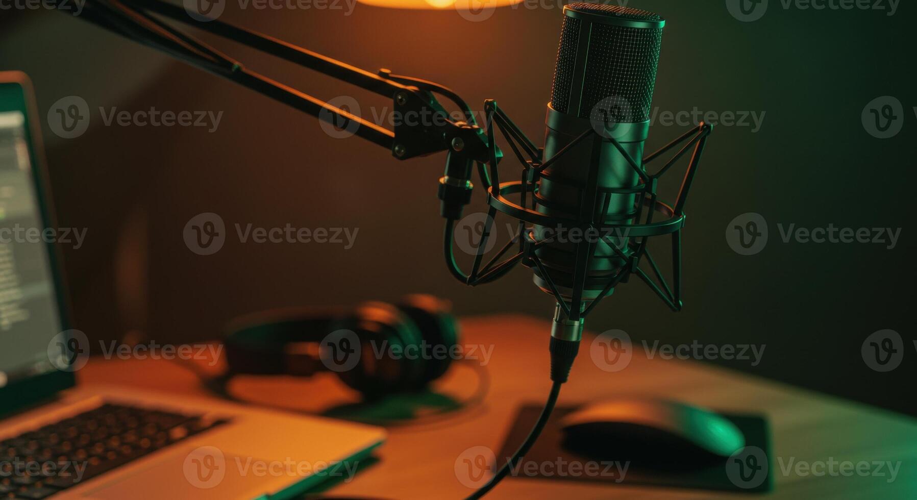 Professional condenser microphone on a boom arm over a desk with a laptop, headphones, and mouse. Studio setup for podcasting, streaming, or voice recording. photo