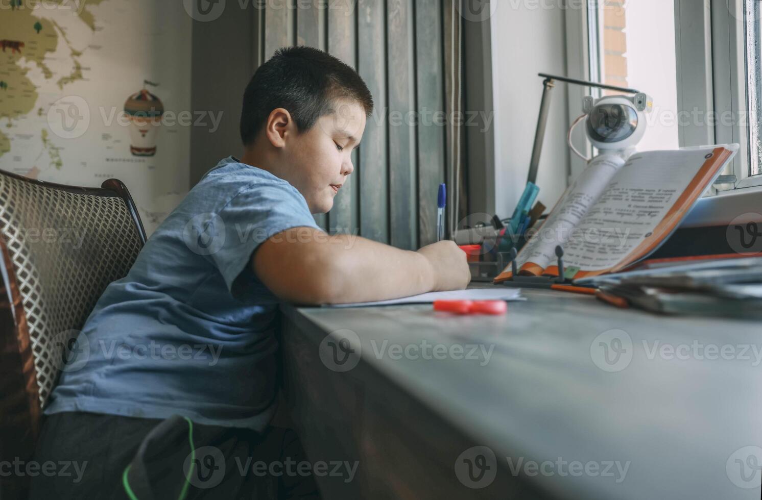 asian boy write in notebook, homework beside open textbook on desk, study tool, education, homeschooling, parenting resource photo