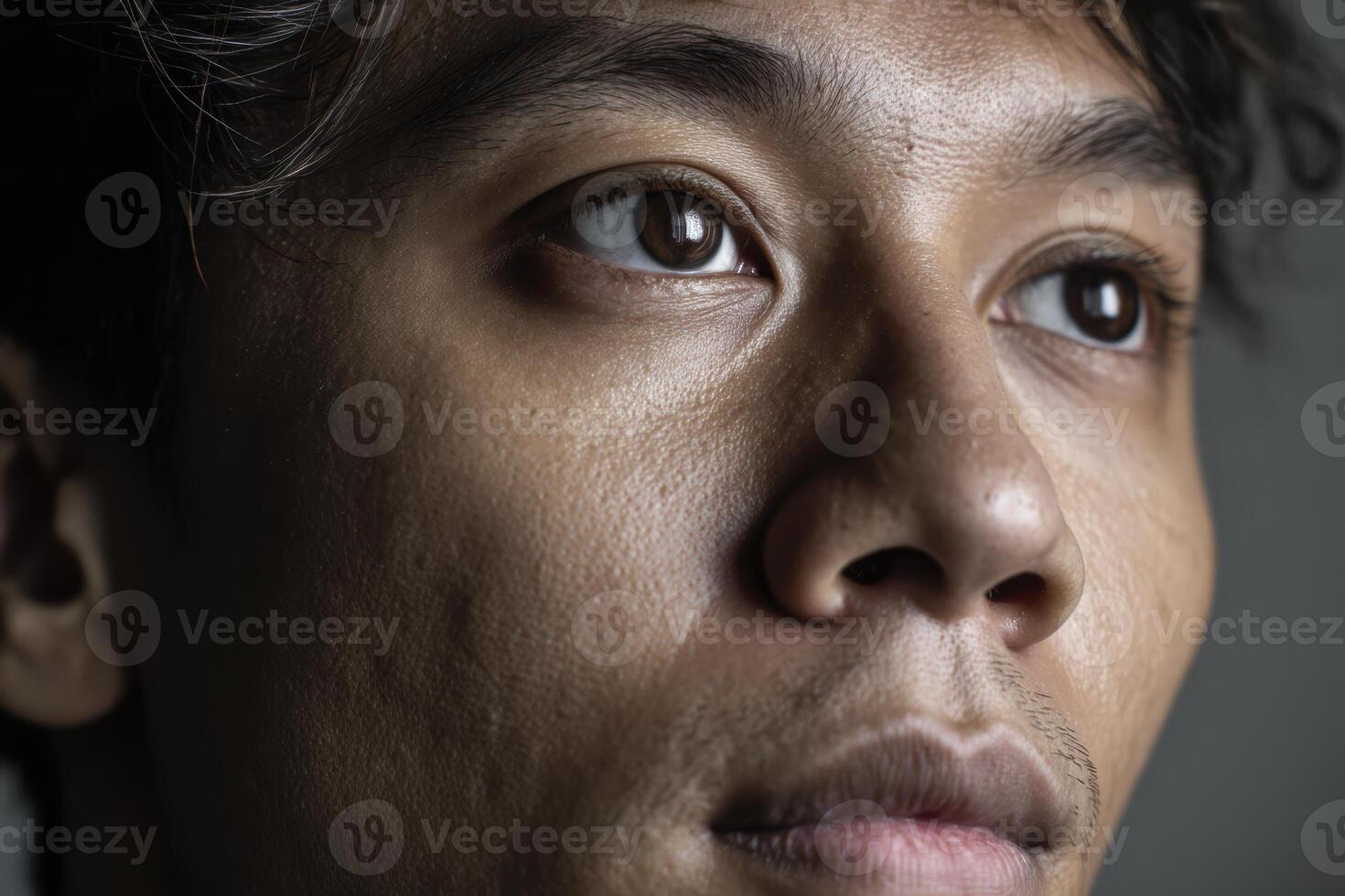 Close-up of a contemplative person with short hair. Soft lighting accentuates facial features including deep brown eyes, textured skin, and slight stubble. Expression appears thoughtful photo
