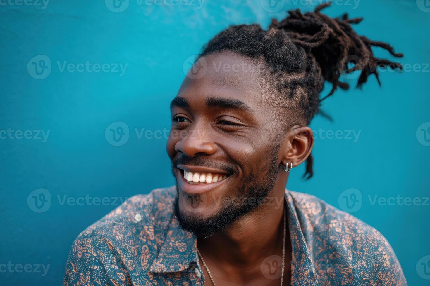 Smiling person with dreadlocks, wearing a patterned shirt, and hoop earring. The individual looks to the side, exuding a joyful and lively expression with vibrant energy photo