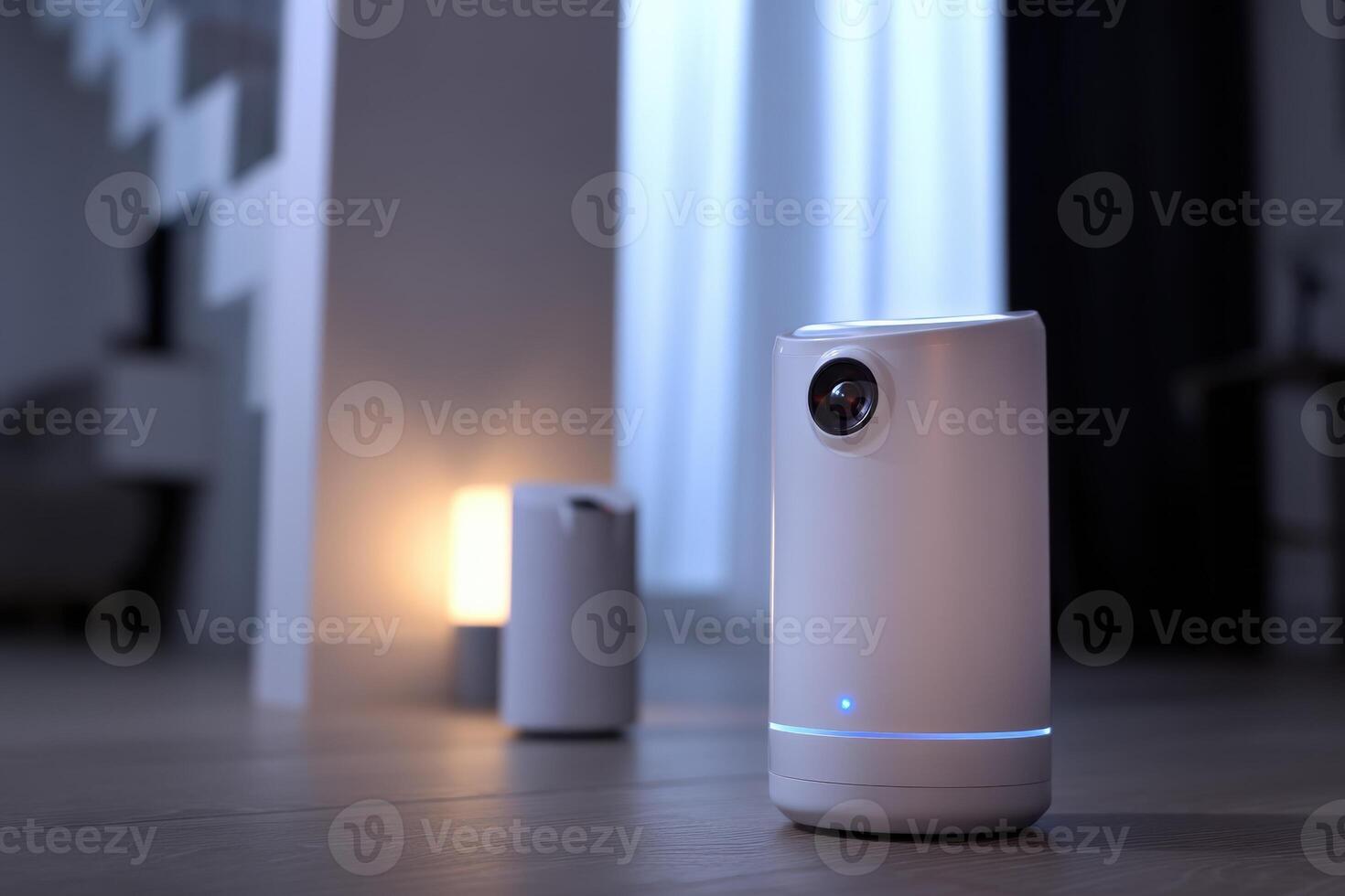 A small cylindrical security camera with a visible lens sits on a wooden floor indoors. Another similar device glows softly in the background, both near a staircase photo