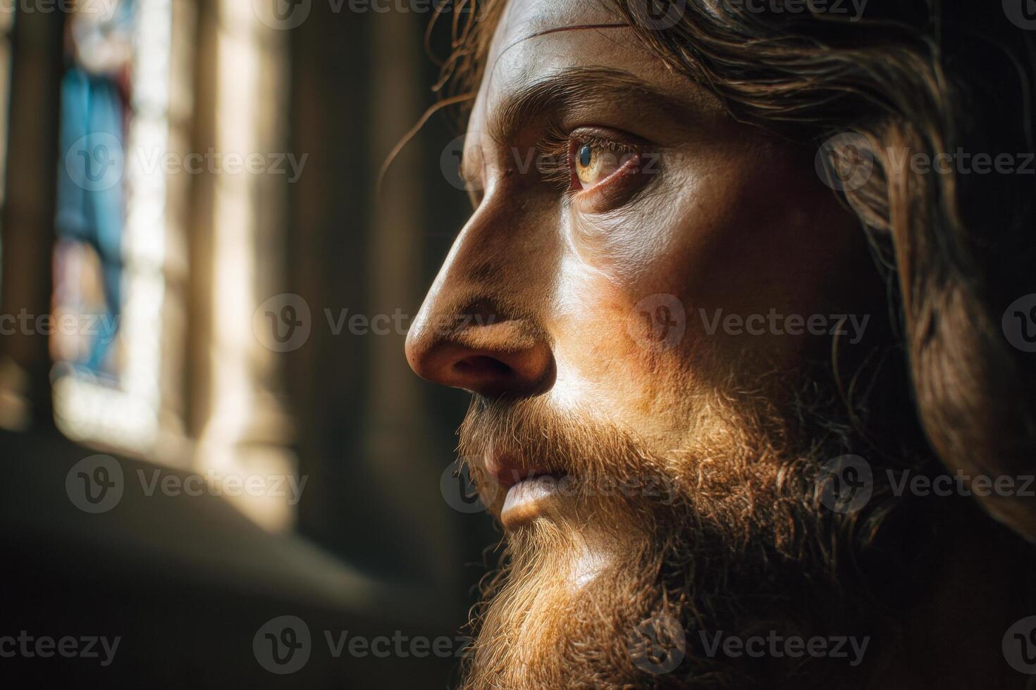 Detailed close-up of a statue's face with strong natural light highlighting its features, showcasing a bearded figure gazing solemnly. A blurred stained glass window appears in the background photo