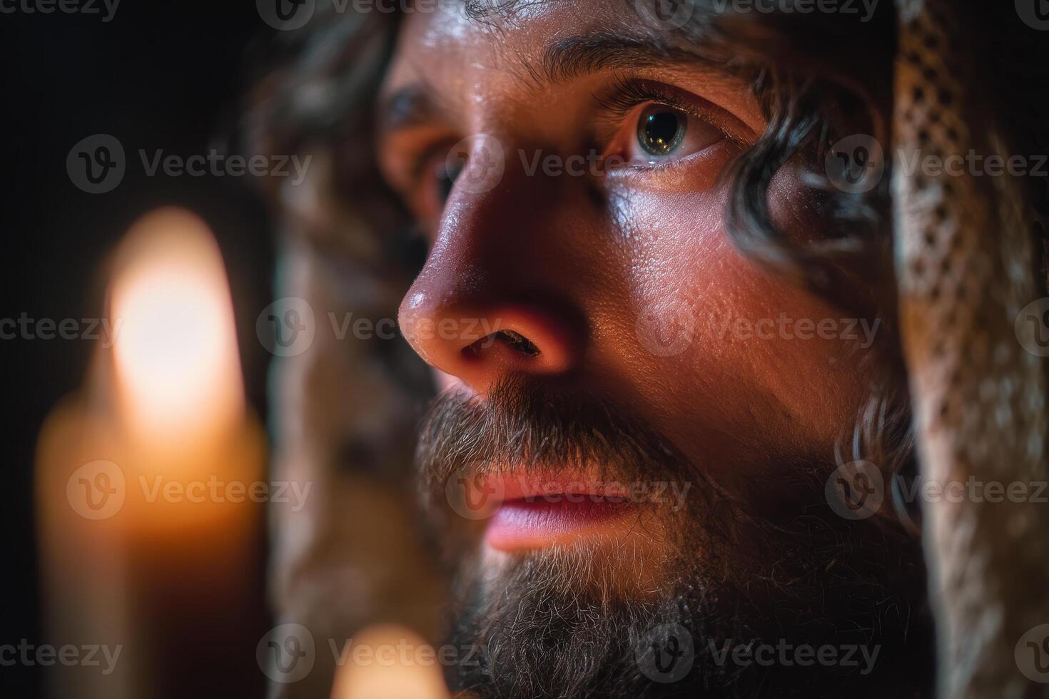 Curly-haired person with a beard gazes contemplatively. Warm candlelight casts a soft glow, creating a serene and introspective mood, highlighting facial features and textures photo