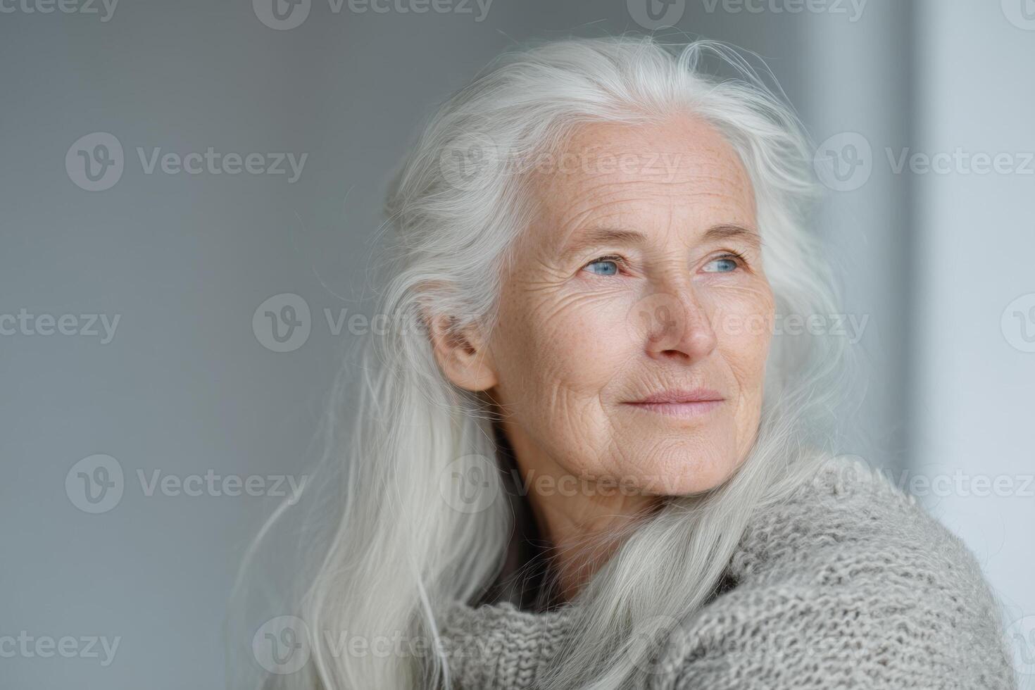 Serene woman with long white hair gazes thoughtfully to the side, wearing a textured gray sweater. Her expression is gentle and peaceful, capturing a moment of calm contemplation photo