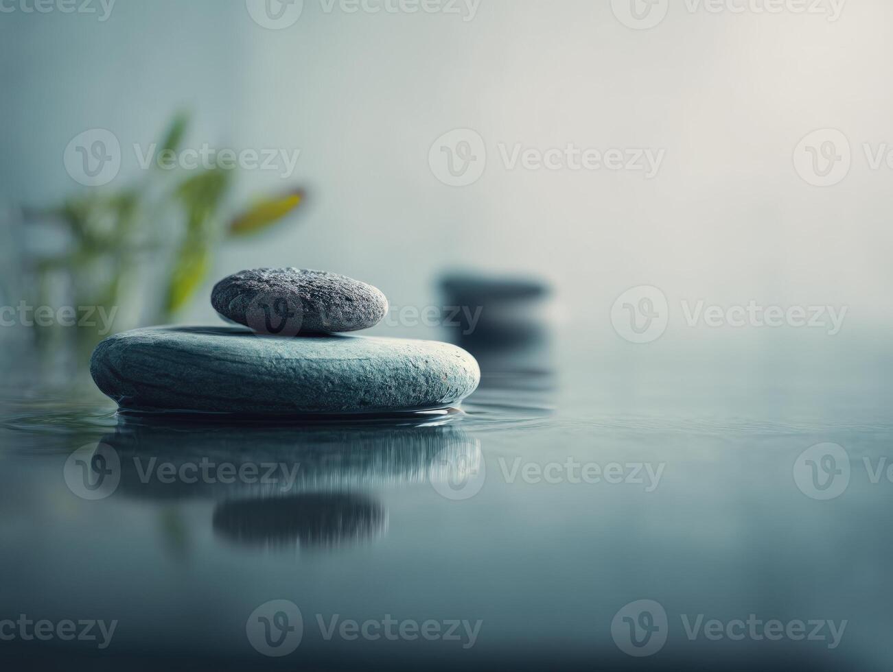 Smooth stones are delicately stacked on a calm water surface with gentle ripples. Soft focus plants are visible in the background, creating a serene and tranquil ambiance photo