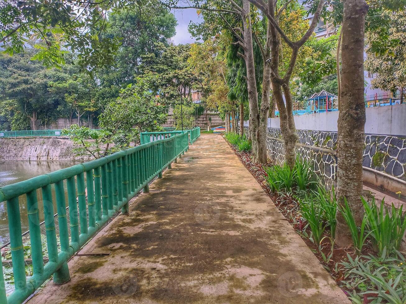 Pathway with green railings surrounded by trees and water body. photo