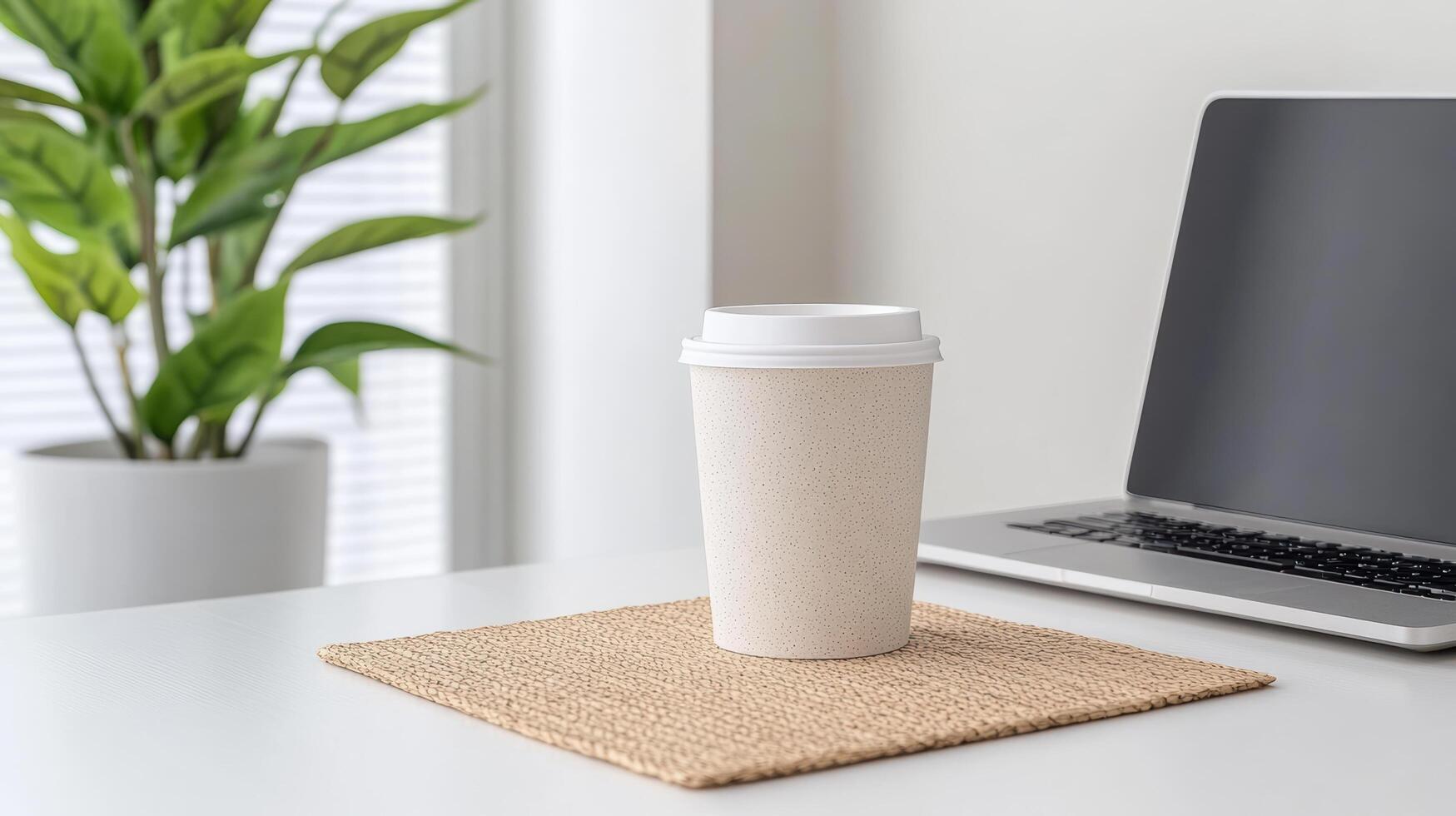A coffee cup on a table with a laptop and a plant photo