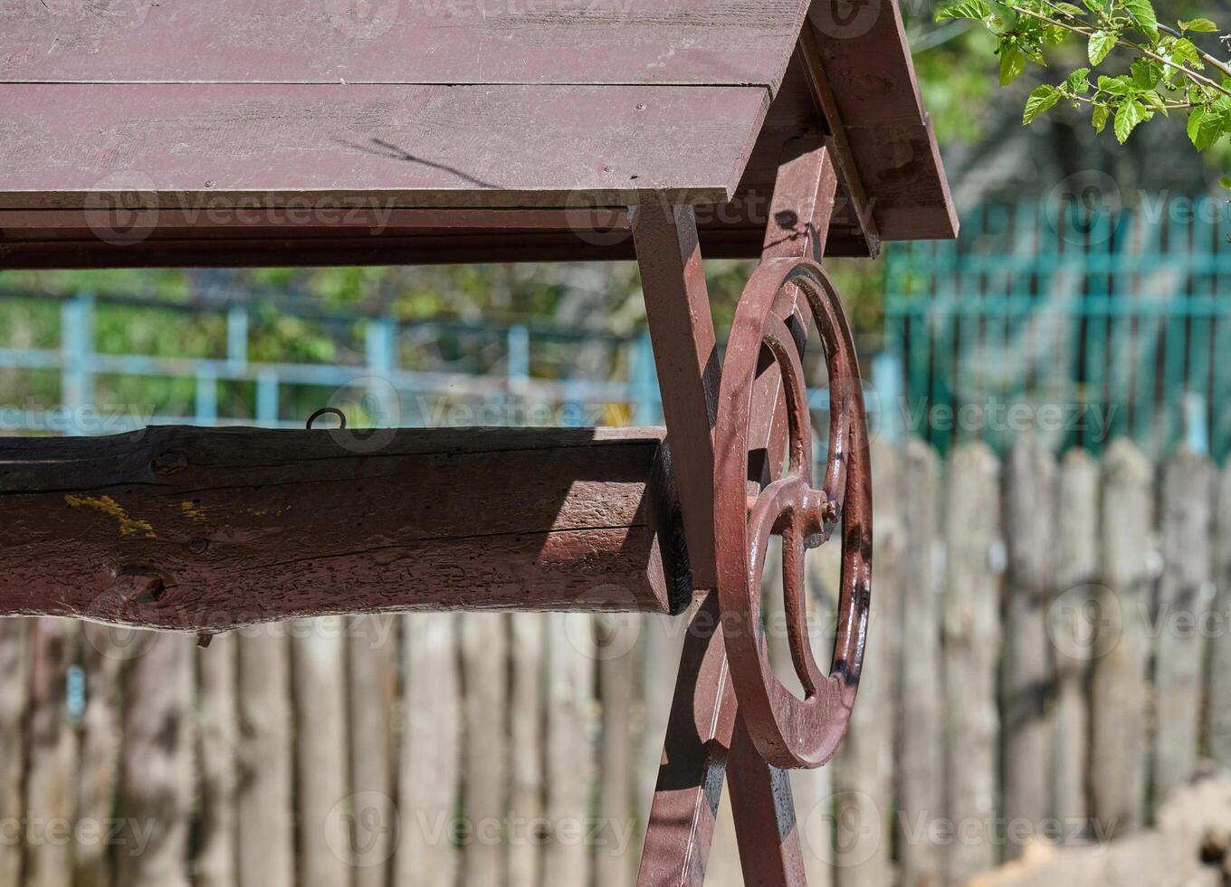 Vintage wooden water well with a hand crank and weathered roof, set against a rustic wooden fence and garden background photo