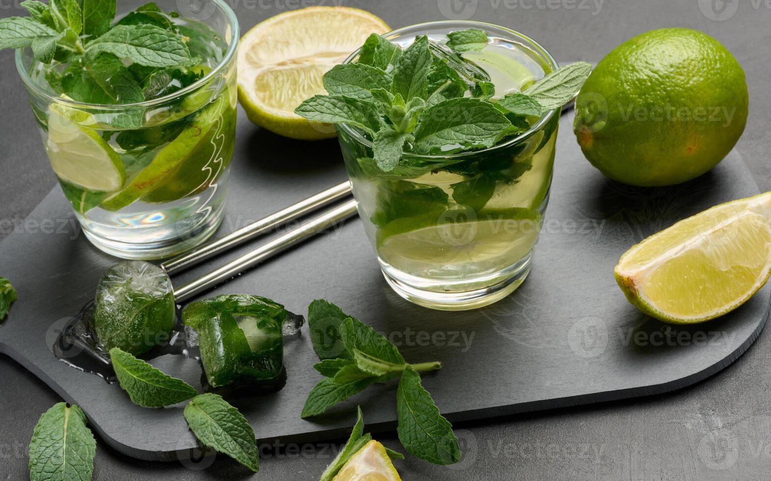 Glass of mojito cocktail with fresh mint leaves, lime slices, and ice cubes on a dark stone background. Top view photo