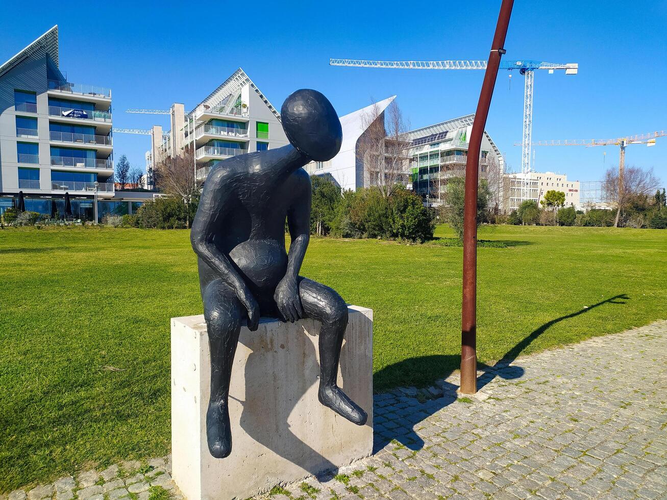 LISBON, PORTUGAL - JANUARY 17, 2025 Modern art sculpture in park setting. Abstract figure contemplates urban development. Symbolism of change, reflection, or solitude. photo
