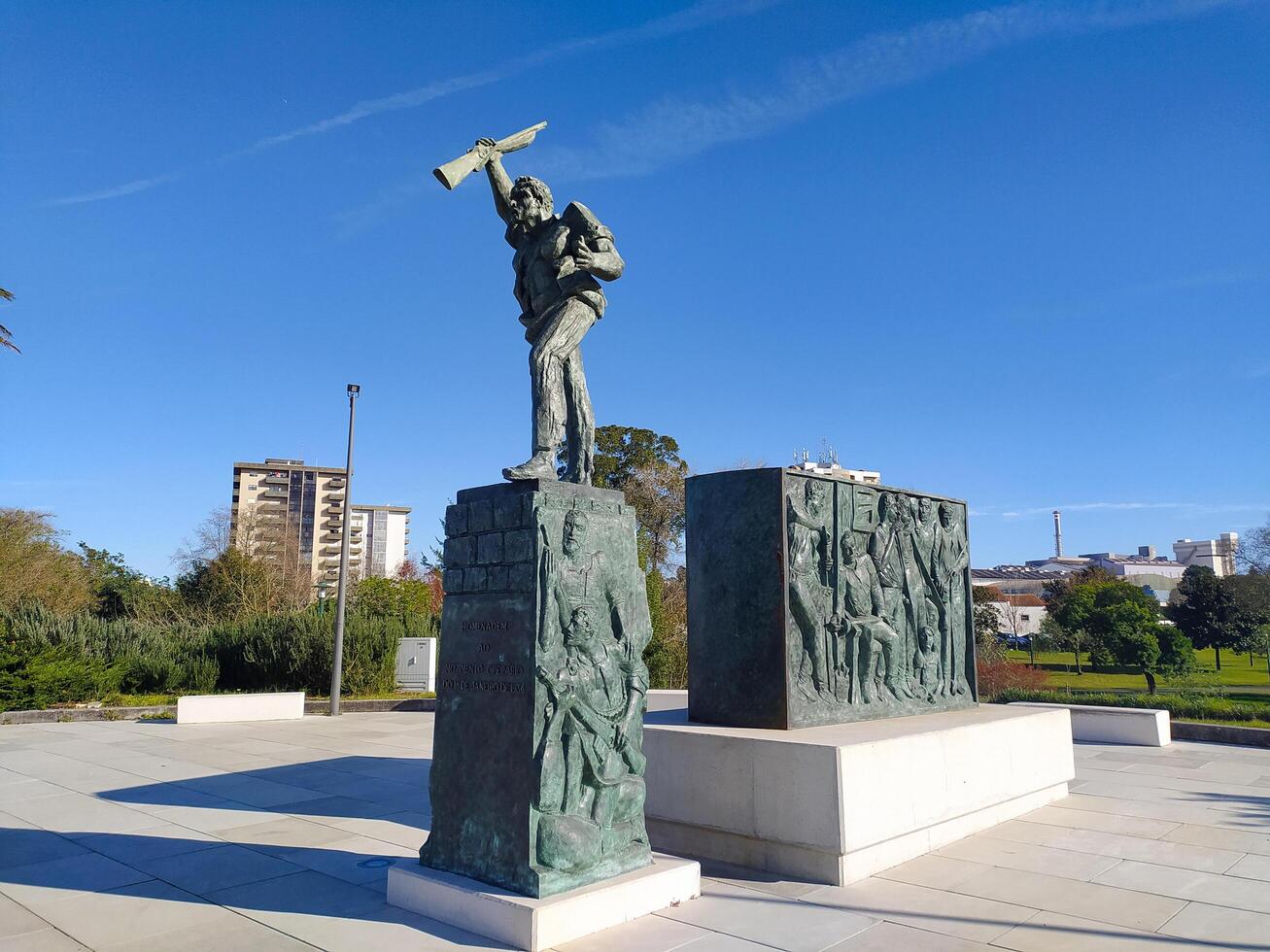 MARINHA GRANDE, PORTUGAL - JANUARY 14, 2025 Monument honoring glassworkers, bronze sculpture, featuring reliefs, set against blue sky and cityscape. Editorial use. photo