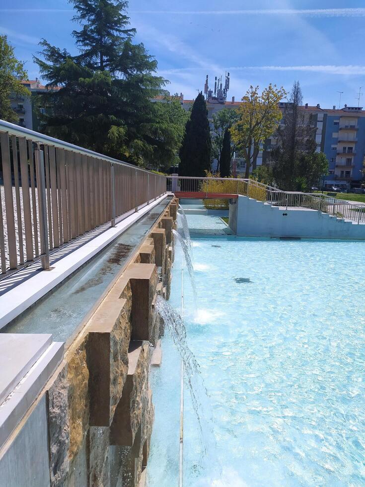 ALCOBACA, PORTUGAL - APRIL 27, 2025 Cascading water feature in a modern park setting. Blue water contrasts with stone textures under a clear sky. Tranquil, architectural detail. photo