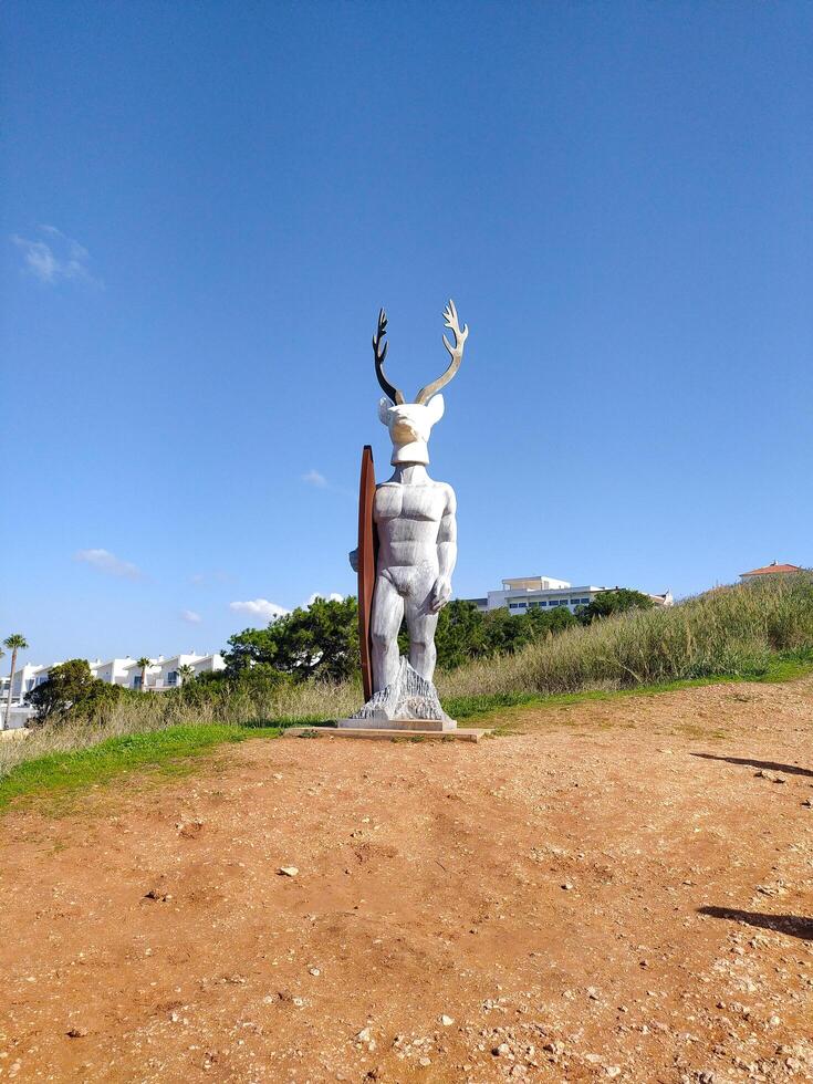 NAZARE, PORTUGAL - NOVEMBER 02, 2024 Statue depicting a human figure with antlers and a surfboard at a coastal location. Conceptual art, travel destination. photo
