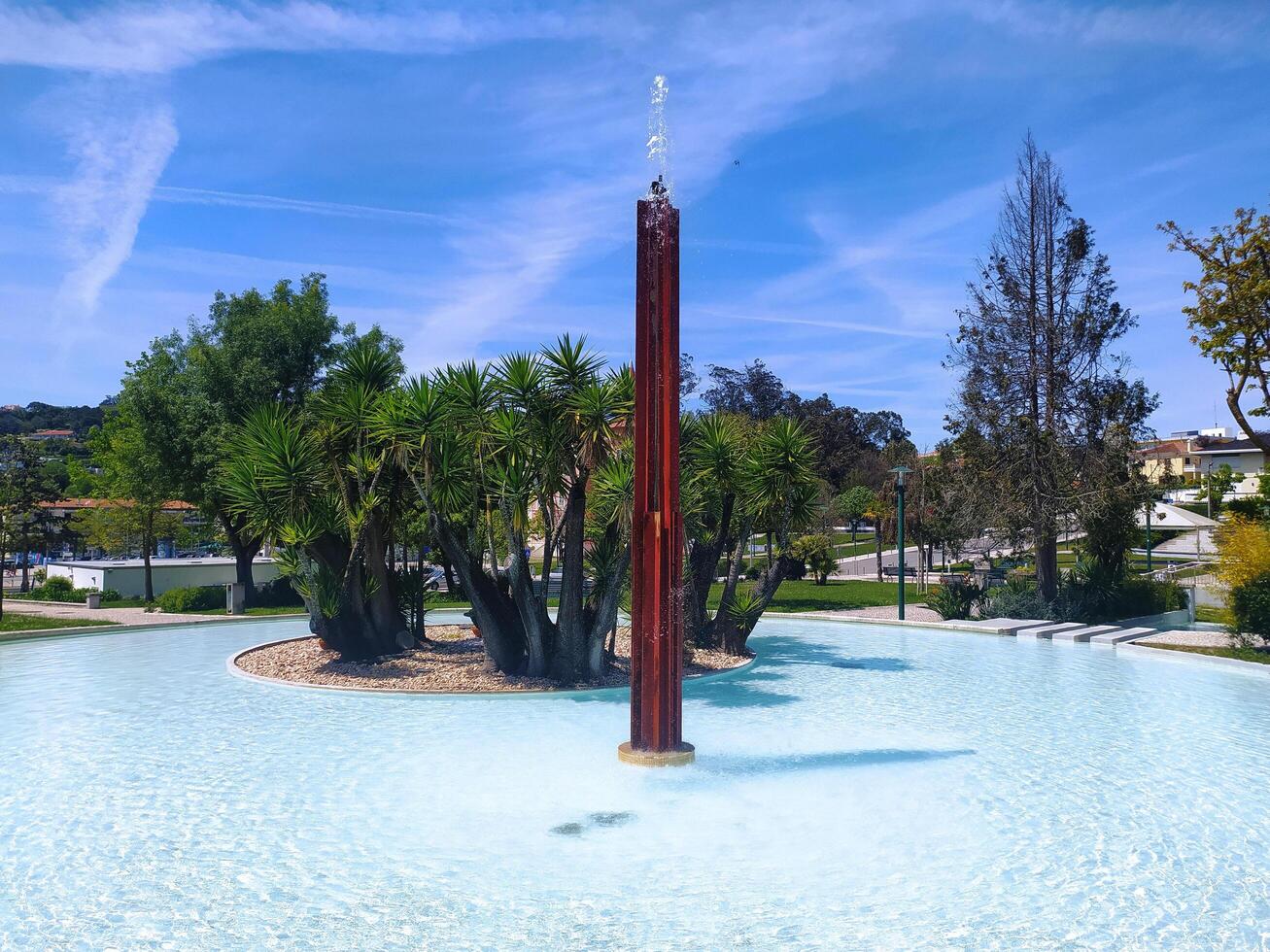 ALCOBACA, PORTUGAL - APRIL 27, 2025 A tranquil scene shows a stylized fountain in a park-like setting. The mood is calm, with blue sky and water. Landscaping is pleasant. photo