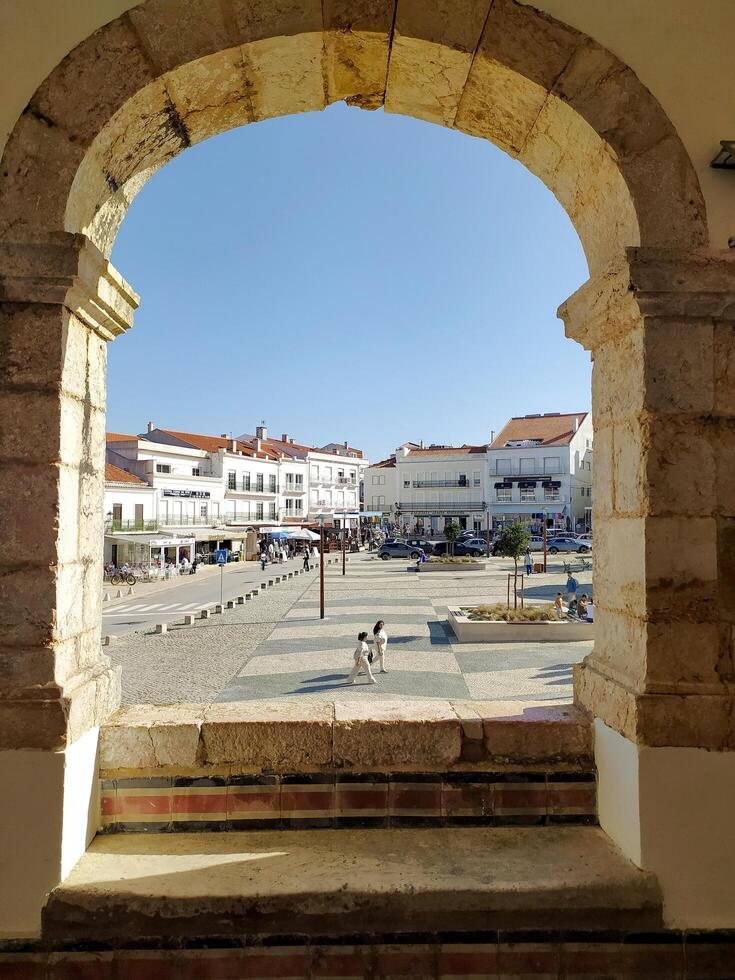 NAZARE, PORTUGAL - NOVEMBER 02, 2024 View of town square framed by stone archway. People walk in distance on a sunny day. Travel and architecture related content. photo