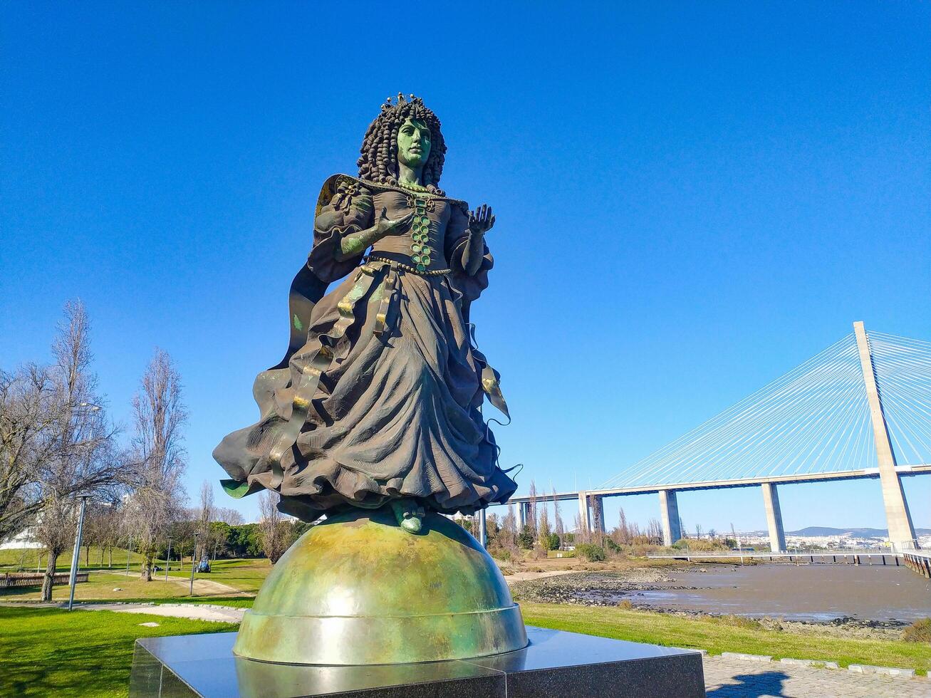 LISBON, PORTUGAL - JANUARY 17, 2025 Bronze statue of Queen surrounded by parkland with distant bridge. Travel, history, culture concepts. Editorial use. photo