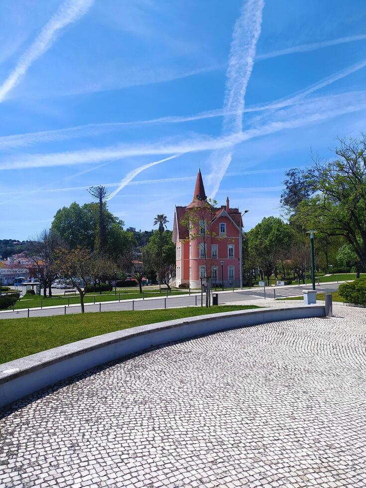 ALCOBACA, PORTUGAL - APRIL 27, 2025 Pink building with conical roof in a park setting under a bright blue sky marked with contrails. Urban landscape, peaceful mood. photo