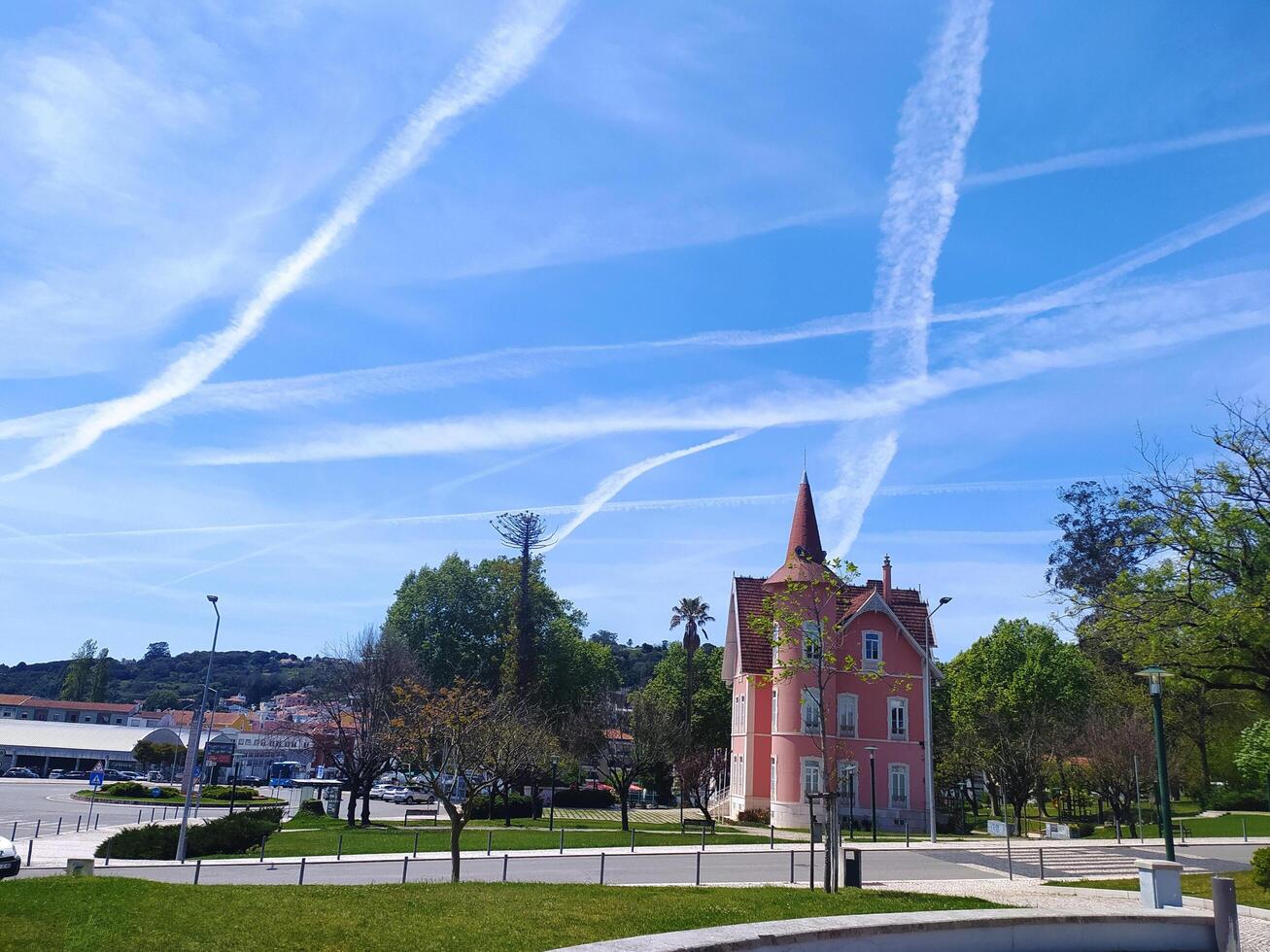 ALCOBACA, PORTUGAL - APRIL 27, 2025 Quaint building with a pointed roof, juxtaposed against a bright blue sky crisscrossed with prominent contrails. A sunny, outdoor setting. photo