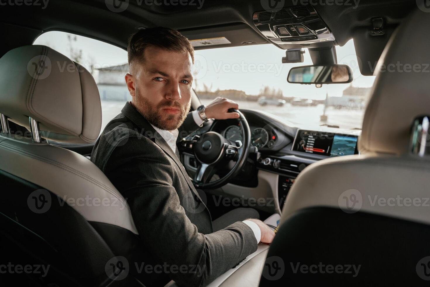 Looking behind at the camera. Man in black suit is sitting in the car,,, driving photo