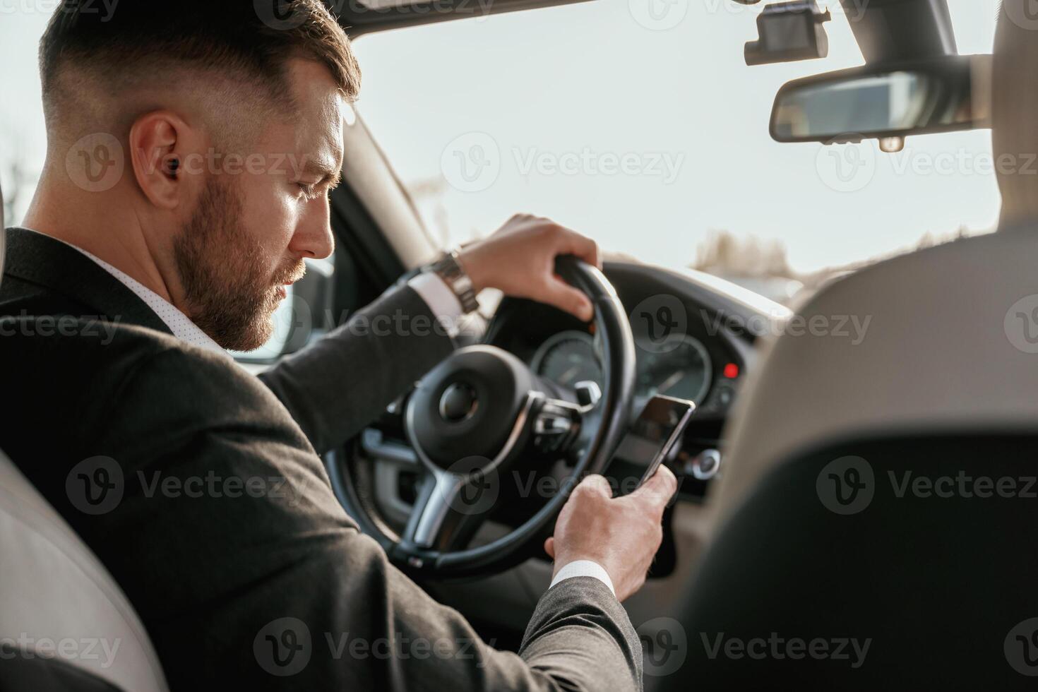 Surfing the internet by using smartphone., Man in black suit is sitting in the car, driving photo