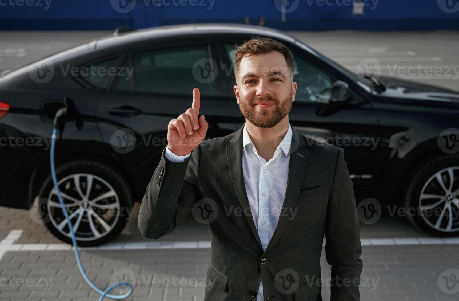 Having, an idea, showing finger up. Businessman in suit is near his black car outdoors photo