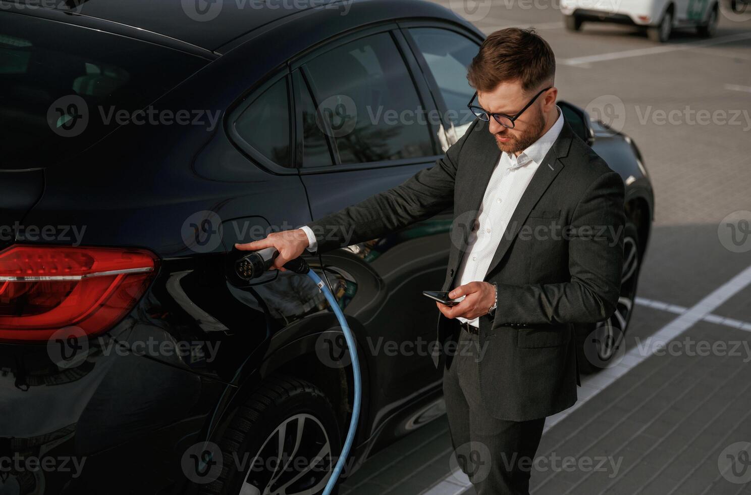 Green, energy concept, charging. Businessman in suit is near his black car outdoors photo
