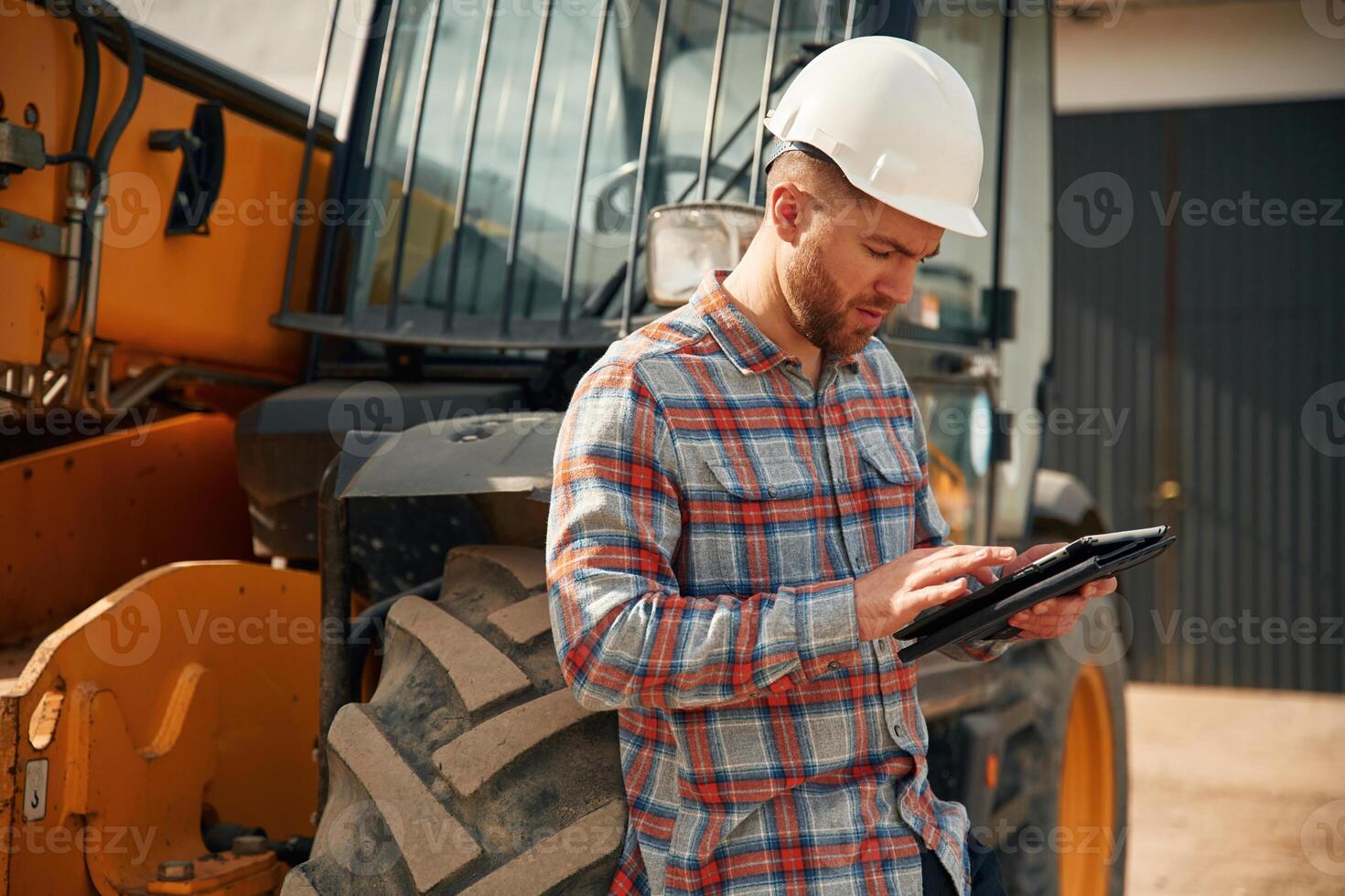 Digital tablet in hands. Man ,is with, tractor. Agricultural worker photo