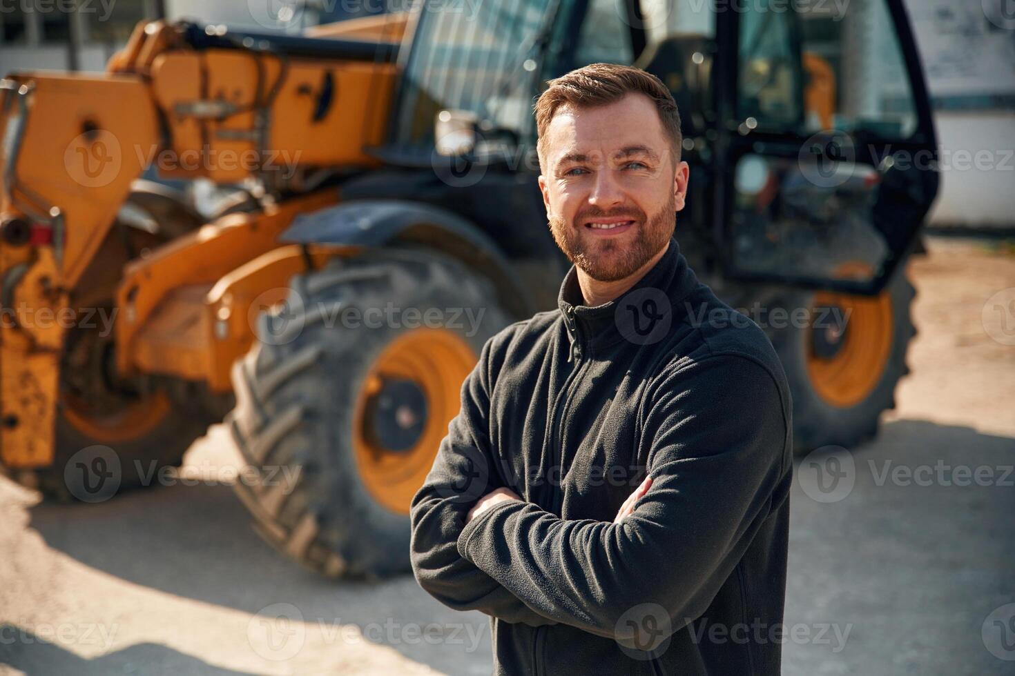 In black hoodie.. Standing and posing. Man is with tractor. Agricultural worker photo