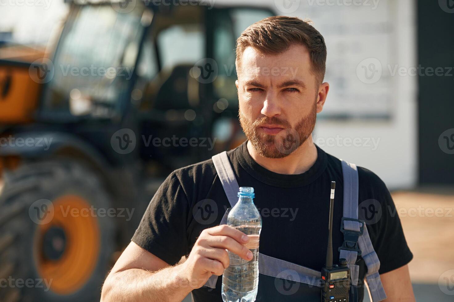 Bottle of water, drinking, taking, a break. Man is with tractor. Agricultural worker photo