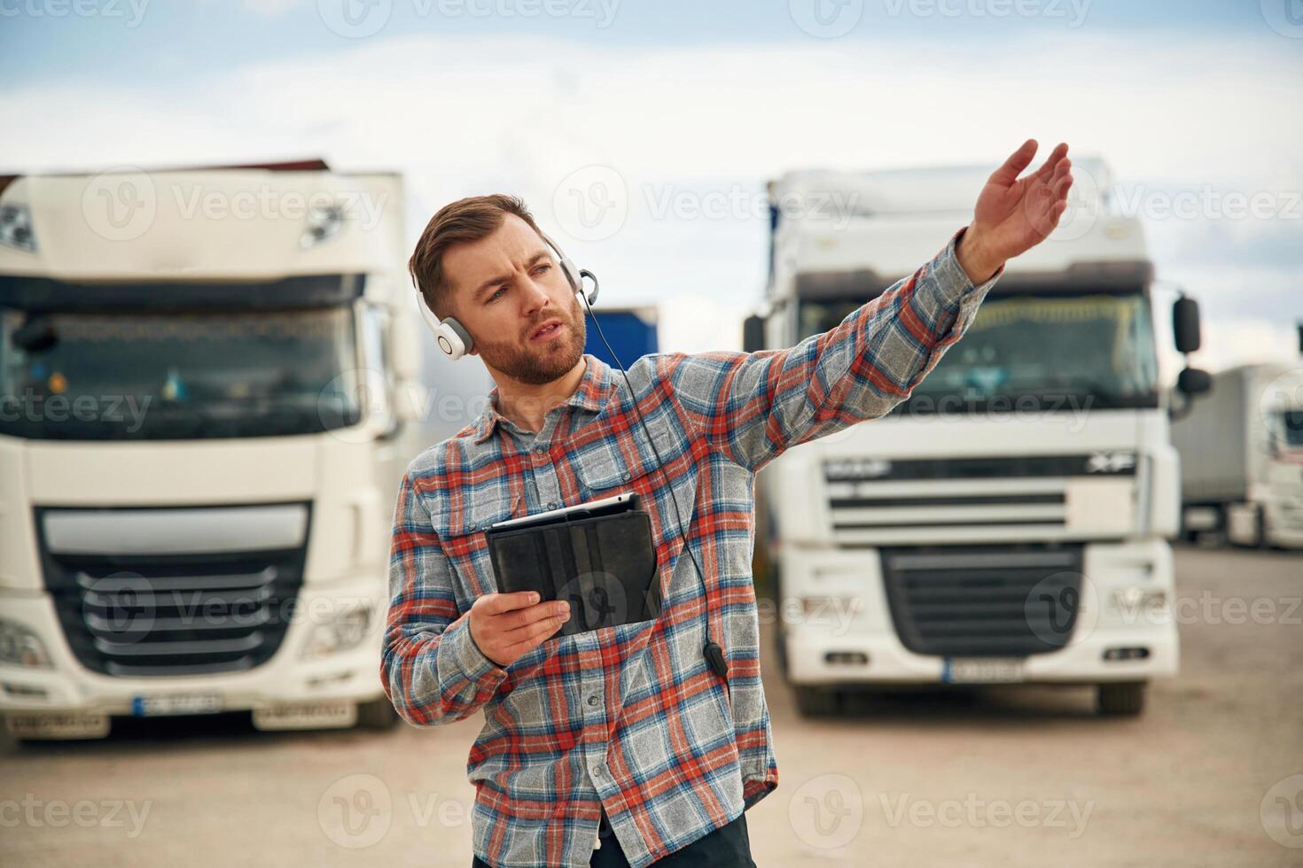 Showing, the way, with tablet. Man is standing against trucks outdoors photo