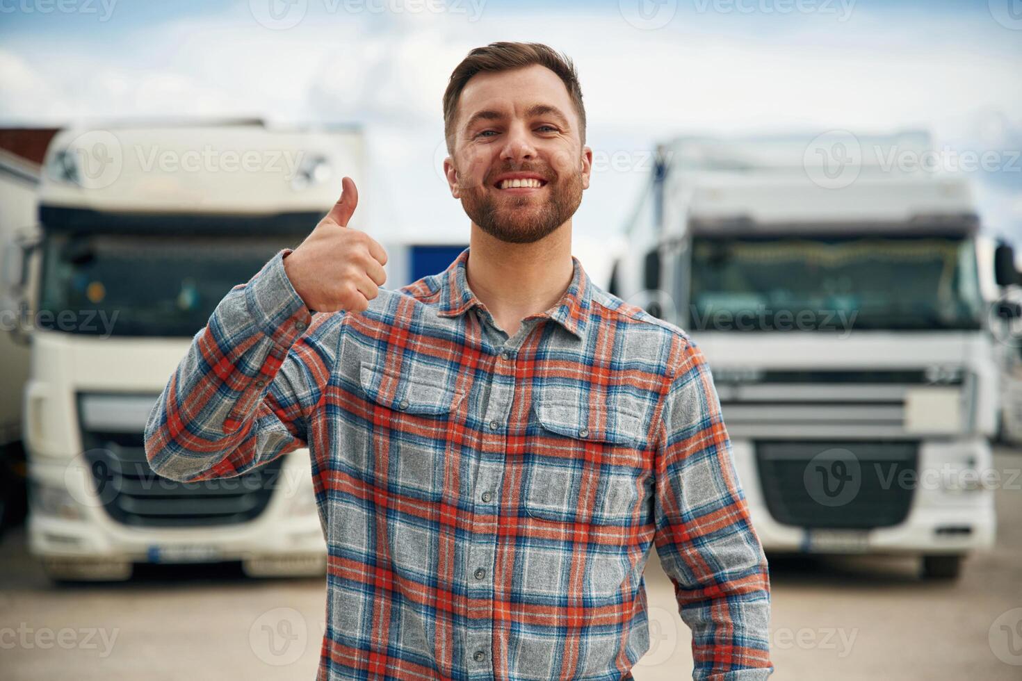 Showing thumb up and smiling. Man is standing against trucks outdoors photo