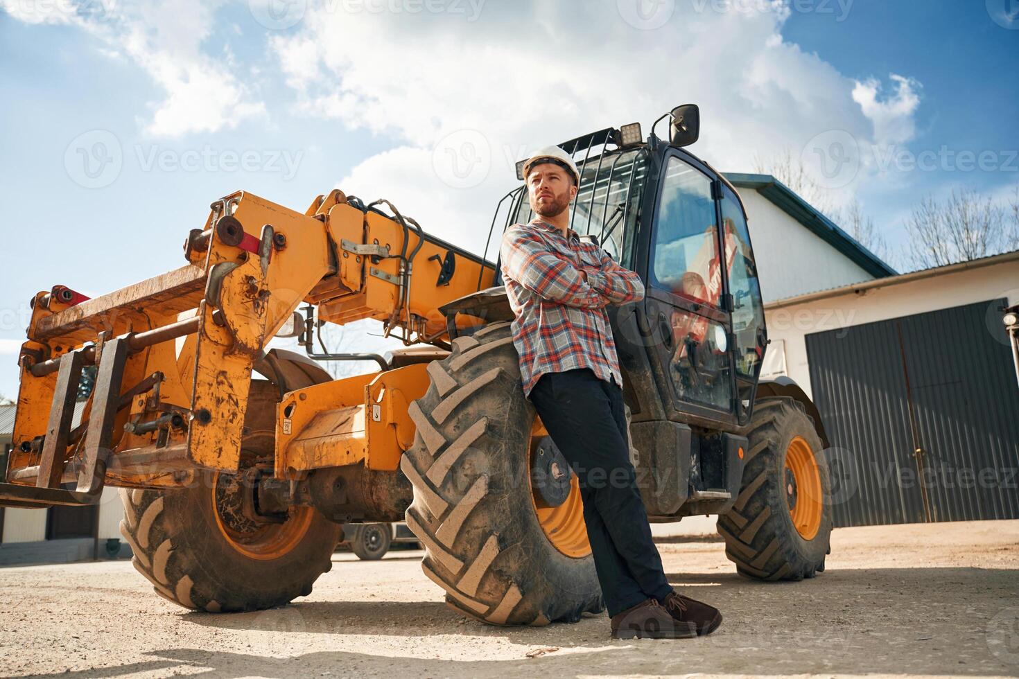 With ,arms crossed. Man is with tractor. Agricultural worker photo