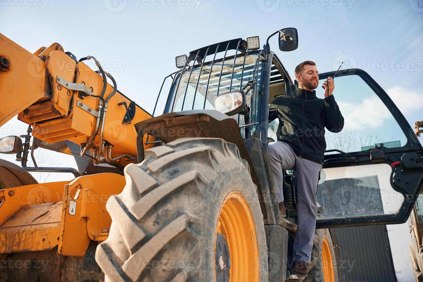View from, below, using walkie talkie. Man is with tractor. Agricultural worker photo
