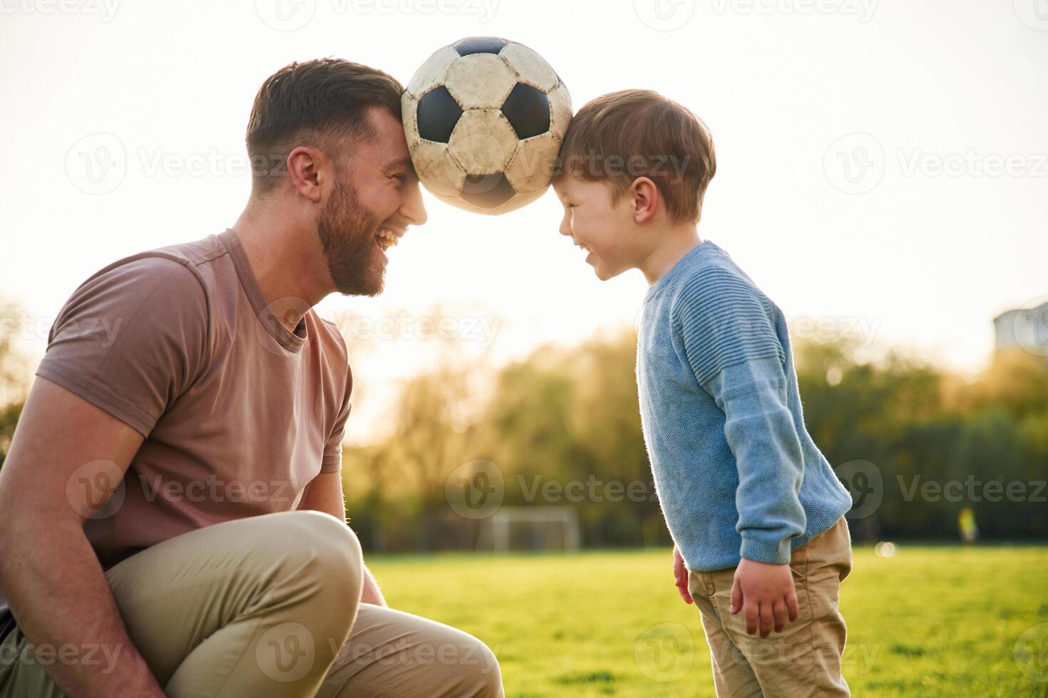 Soccer ball, holding it by heads, fun. Happy father with son are on the field at ,,summertime photo